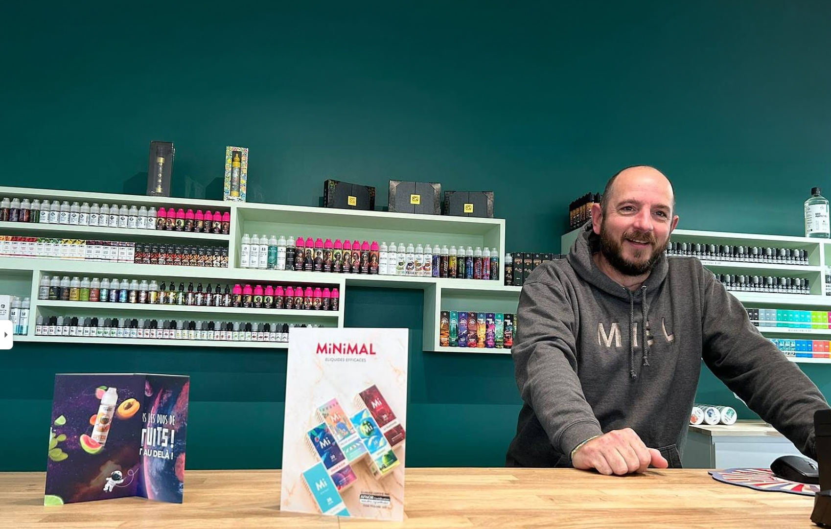 Fred, conseiller, derrière le comptoir en bois de la boutique, devant les rayonnages d’e-liquides.