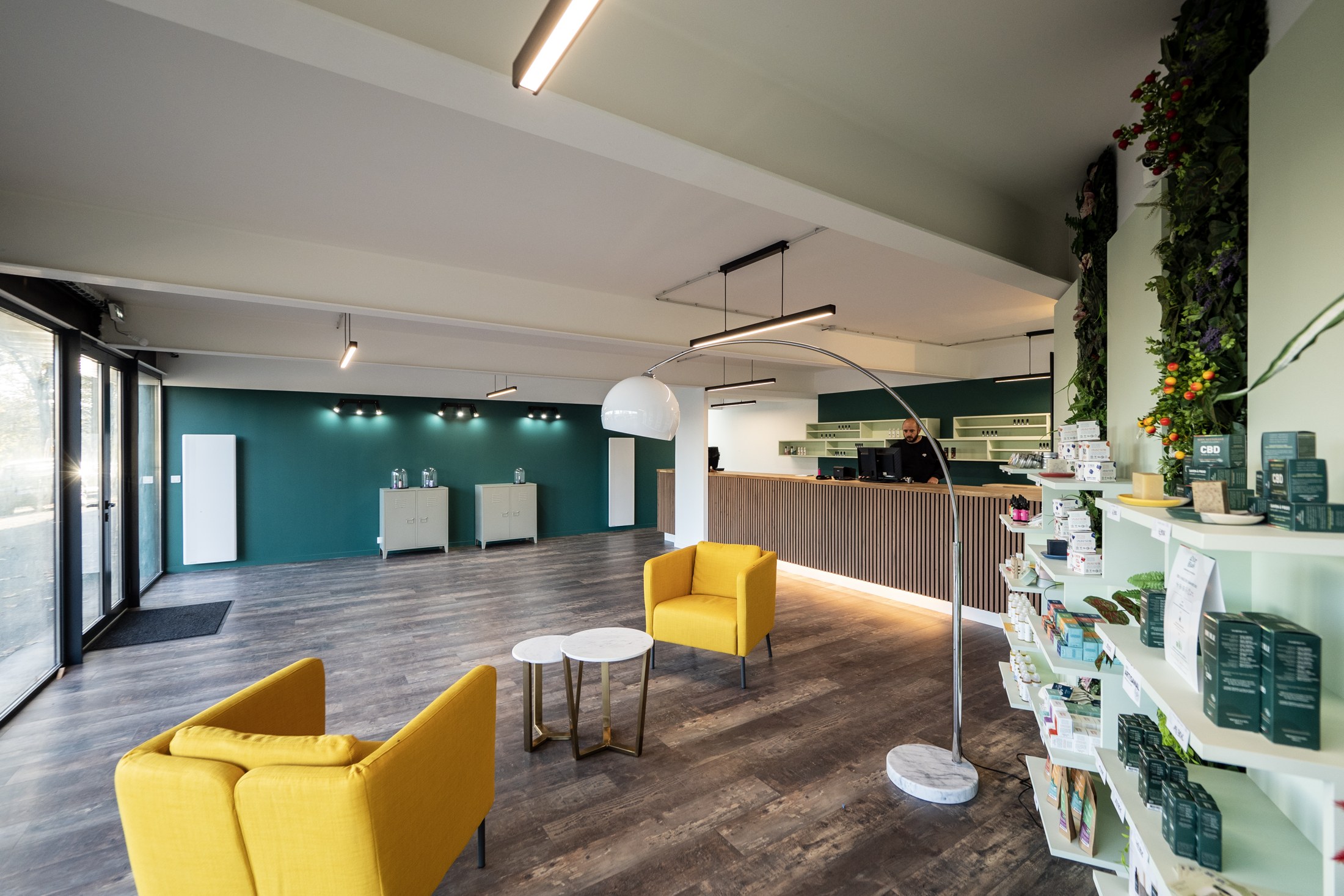 L’espace de la boutique : fauteuils moutarde, table basse, comptoir en bois et mur végétal.